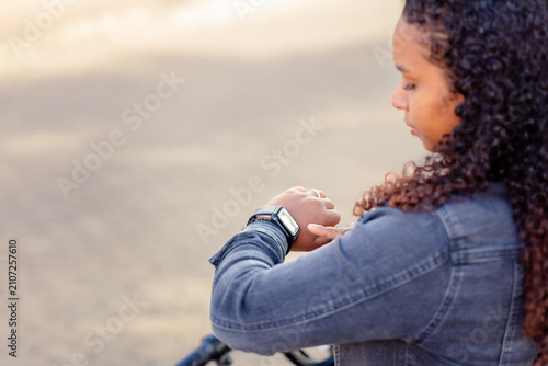 Young Black woman checking her smartwatch outdoors, representing wearable technology and an active daily lifestyle.