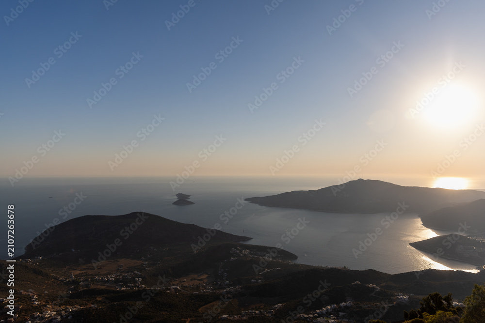 Fototapeta premium Golden sunset bathes a tranquil coastline and calm sea, with silhouetted hills and distant islets creating a peaceful, expansive horizon ideal for travel, nature, and landscape photography. Turkey