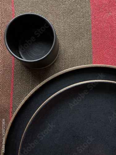 Close-up of black ceramic plates and cup on natural linen textile. Handmade stoneware tableware with minimalist design and neutral tones for home decor, dining and interior concepts.