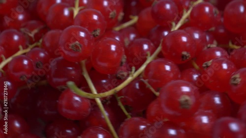 Extreme close-up of ripe red currants rotating on a turntable, highlighting their juicy, translucent berries and green stems under bright lighting.