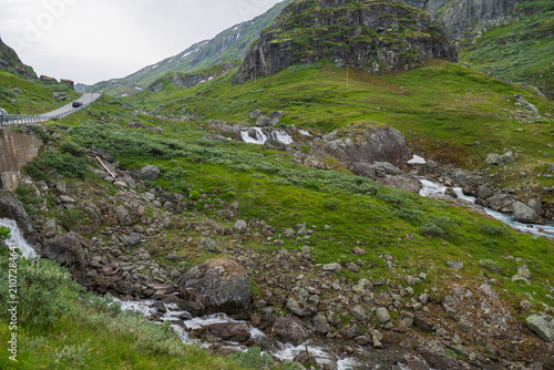 Cascading waterfalls and rocky creek winding through lush green slopes near Geiranger, Norway.