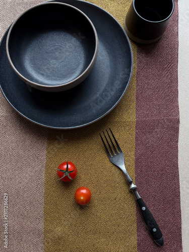 Black ceramic bowl and plate with cherry tomatoes on linen textile. Handmade stoneware tableware in a minimalist setting with natural textures for dining, kitchen, home decor and lifestyle concepts.