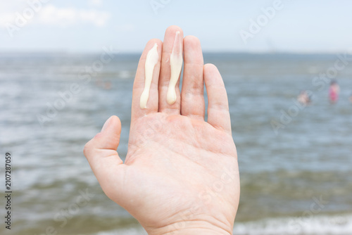 Closeup of a man applying the correct amount of sunscreen for face and neck - two fingers - on a beach. 