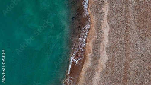Top-down aerial view of Eastbourne's pebble beach, emerald shoreline and coastal road, revealing striking natural patterns and urban geometry along the East Sussex coast, England.