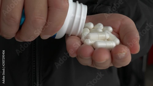 Close-up of a hand pouring white medical capsules from a bottle into an open palm, highlighting the daily health routine under soft lighting.