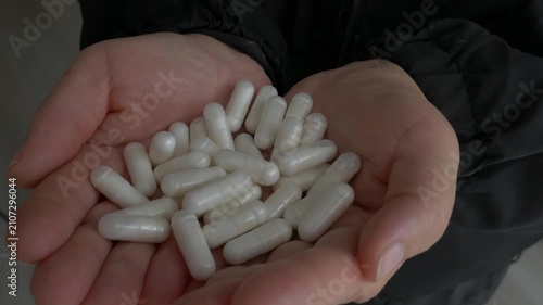 Close-up of human cupped hands holding a large pile of white medical capsules, showcasing healthcare, supplements, and wellness treatment.