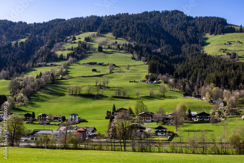 Tyrolean Brixental valley - view of a spring lush green hillside with farms and a blue sky