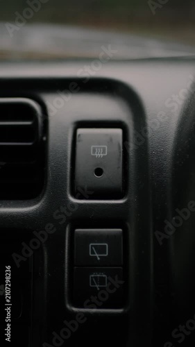 Close-up of a finger turning off the rear window defroster button on a car dashboard. Vehicle interior scene representing climate control, driving safety, and convenience.