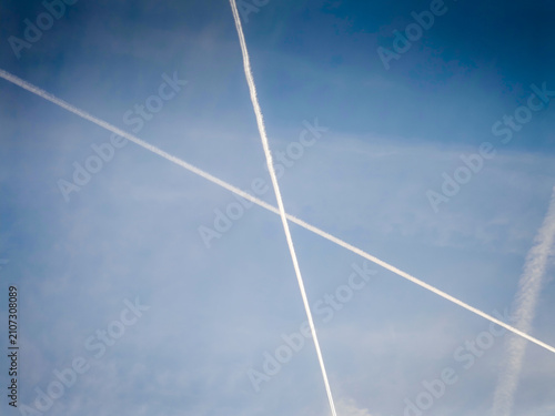 Bild auf Leinwand Airplane contrails crossing a clear blue sky, white vapor trails creating an abs