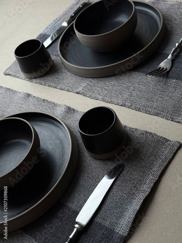 Modern black ceramic dinnerware arranged with cutlery on natural linen textile. Minimal dining composition with neutral tones, suitable for hospitality, home decor and lifestyle concepts.