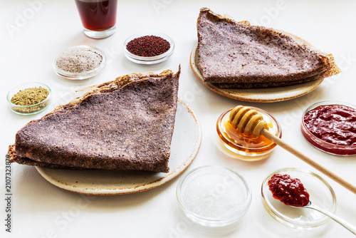 Close-up of ragi-based crepes (made from finger millet), with small bowls containing whole ragi and ragi ground into flour, along with a few ingredients served alongside the crepes