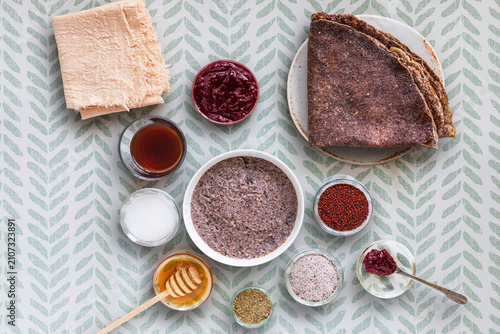 Close-up of pancakes and a dessert made with ragi (finger millet), featuring small bowls containing whole ragi and ragi ground into flour, along with a few ingredients to accompany the pancakes