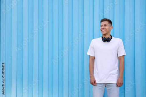 Cuadro en lienzo Young man wearing stylish clothes and headphones near light blue wall outdoors,