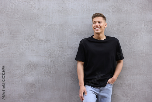Obraz na płótnie Young man wearing stylish black t-shirt near grey wall outdoors, space for text