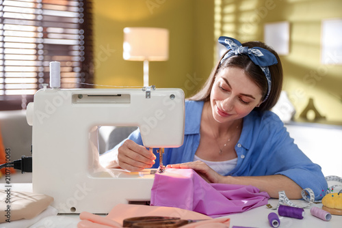 Woman sewing fabric with professional machine at white table in workshop