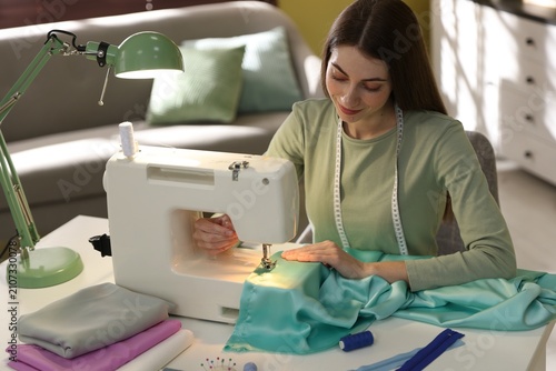 Woman sewing fabric with professional machine at white table in workshop