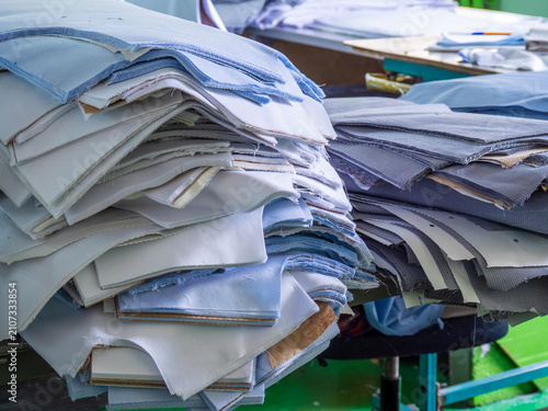 Cuadro en lienzo Large piles of pre-cut blue, white, and grey fabric pieces rest on cutting tables inside a busy garment manufacturing factory