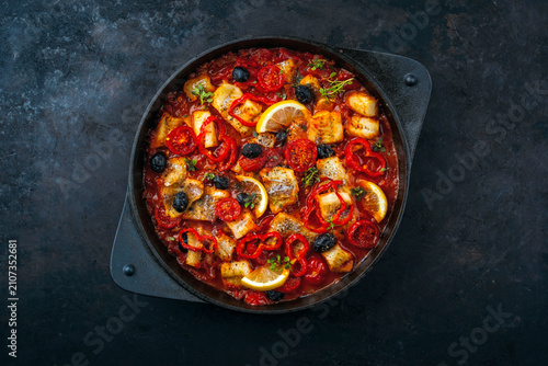 Slow cooked fish stew with tomato souce, vegetable and olives in cast iron casserole