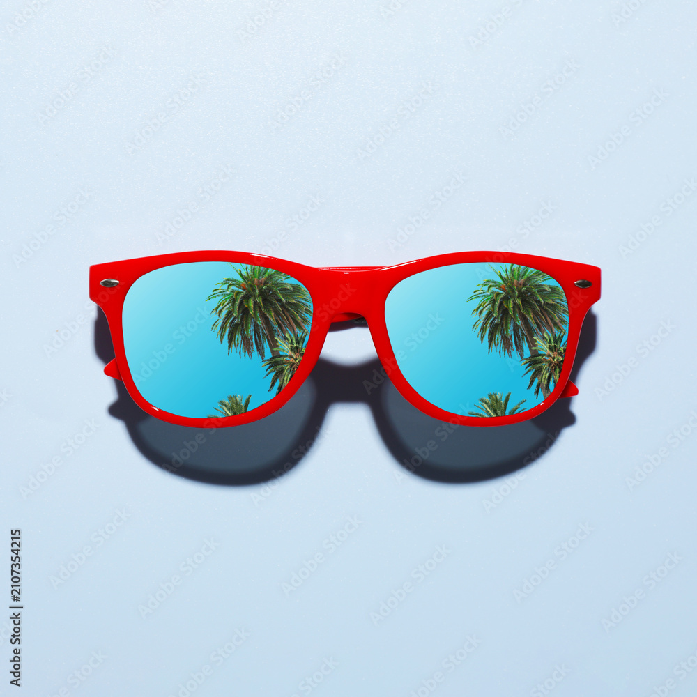 Obraz premium Fashionable sunglasses on light background. Tropical palm trees and blue sky reflecting in lenses