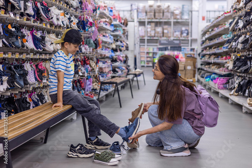 Mother choosing new shoes for her growing son in shoe store. Family shopping, child growth, back to school preparation and smart spending concept