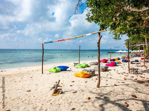 Enjoying a peaceful beach scene with vibrant bean bag chairs arranged on the white sand, offering a comfortable place to relax by the clear turquoise sea under a calm sky in Karimunjawa, Jawa Tengah
