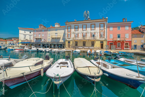 Cres town displaying its historic Venetian architecture and vibrant buildings along the harbor, with numerous boats moored in emerald green Kvarner Gulf under summer sky of Cres Island in Croatia.