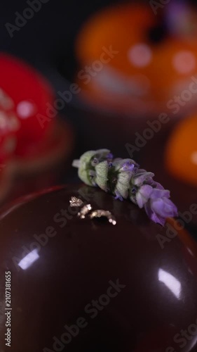 Close up of a beautiful chocolate mousse pastry with a shiny mirror glaze, elegantly decorated with a delicate lavender flower, professional confectionery, cinematic food videography
