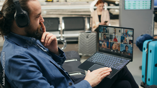 Bild auf Leinwand Businessman on video call using laptop in airport lounge during international travel, participating in virtual meeting with team members and partners