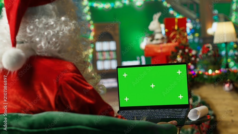 Obraz premium Santa Claus types on a green screen laptop while responding online to children's gift requests and asking what they want for Christmas.