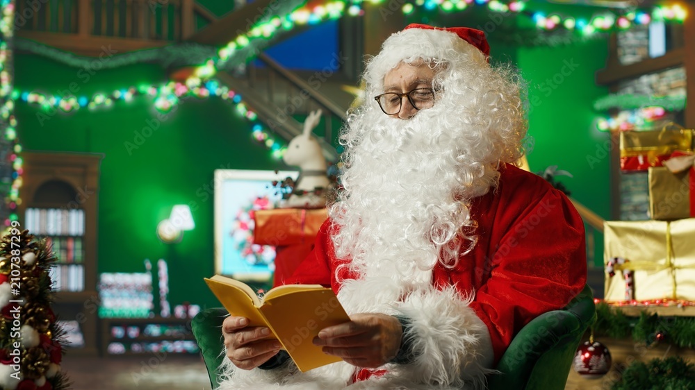 Fototapeta premium Santa Claus reads a book in his workshop after finishing the naughty-or-nice list and before beginning his Christmas trip to visit children.