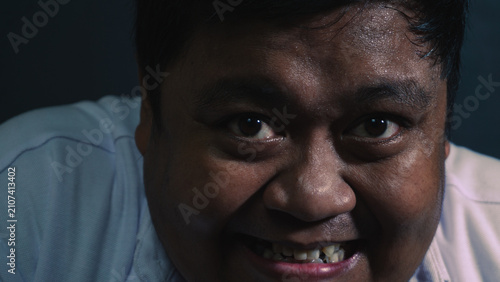 Fotografi A chilling close up portrait captures a disturbed adult Asian male showing a creepy forced smile and wide intense eyes