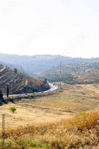 Canvas Print Vertical landscape showing a long curve of a rural highway navigating through a dry, golden-grass valley with surrounding hills
