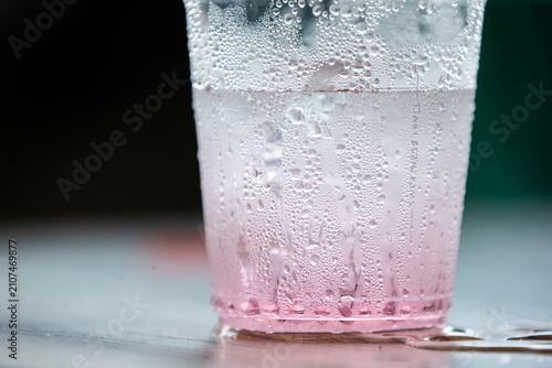 Macro shot of condensation water drops on a plastic cup with pink beverage.   A stunning macro close-up capturing a cold, refreshing pink drink inside a clear plastic cup.