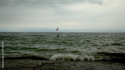 A Canadian flag flies over choppy lake water as waves break along the shoreline. Kew Beach, Toronto, Canada.