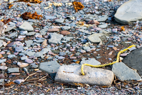 Foto Quebec, Canada, 24 June 2026 : A yellow rope is threaded through a hole in a large rock on a pebbly shore