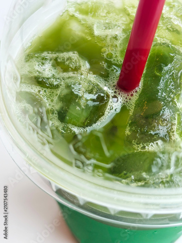 Macro Top View of Refreshing Iced Green Tea Matcha with Red Straw. Extreme macro top-angle shot of refreshing iced green tea matcha with crystal clear ice cubes,