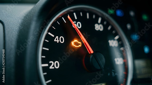 Close-up of car speedometer showing 0 mph with glowing orange check engine light on dashboard