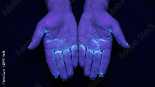 Pair of Hands Held Under Ultraviolet Blacklight Showing Handwashing Hygiene Training