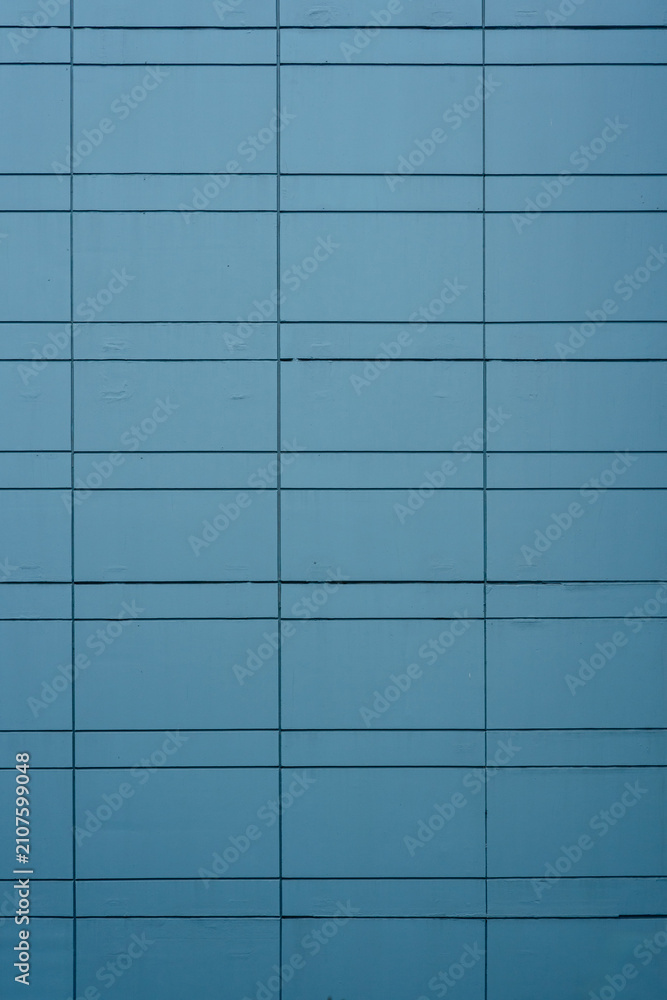 Fototapeta premium Teal blue architectural cladding panels forming a minimalist geometric grid on a modern building facade.