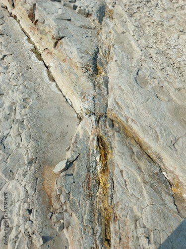 Close-up of a natural gray rock surface featuring weathered textures, cracks, and layered stone formations. Detailed geological background with rugged patterns, ideal for nature, geology, construction