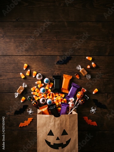 Trick or treat paper bag overflowing with halloween candies and sweets on dark wooden background