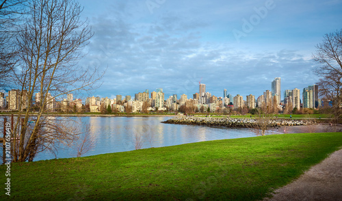 Vancouver city skyline and West End high rise buildings viewed from a green grass lawn in Vanier Park across False Creek under a cloudy blue sky, British Columbia, Canada.