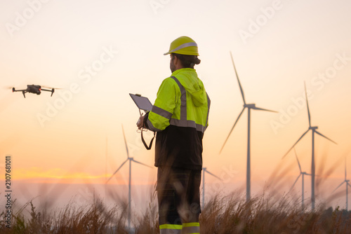 Engineers male flying drone surveying and checking wind turbines from the high angle view of the field during beautiful sunset. using drone technology for work.