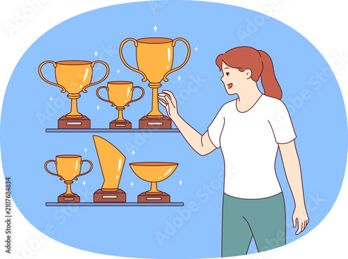Woman leader stands near gold awards and cups won in sports competitions or professional competitions. Girl leader is proud to have trophies earned for outstanding results in business