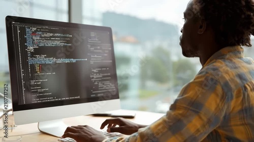 Young male programmer coding on a computer at his desk in a modern, bright office