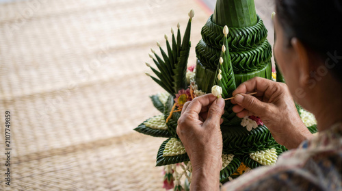 Over shoulder view of senior hands crafting traditional thai folded banana leaf floral arrangement