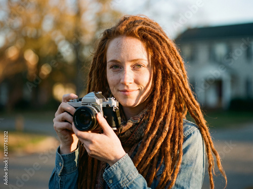 Female photographer with dreadlocks holding vintage camera outdoors in golden hour for portrait and lifestyle background and creative headshot