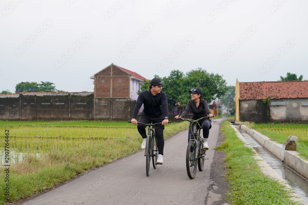 Obraz premium Asian Couple Cycling Through Rural Landscape in Indonesia
