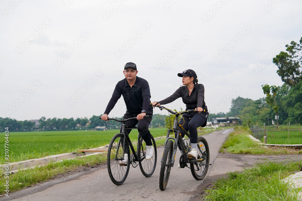 Fototapeta premium Asian Couple Cycling Through Rural Landscape in Indonesia