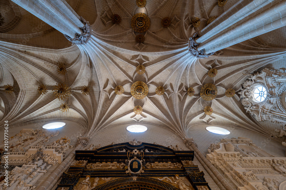 Fototapeta premium Low angle vertical view looking up past the ornate dark marble frame and gilt relief details of the Parish Chapel (Capilla de la Parroquia or San Miguel) entrance toward the gilded boss-adorned gothic